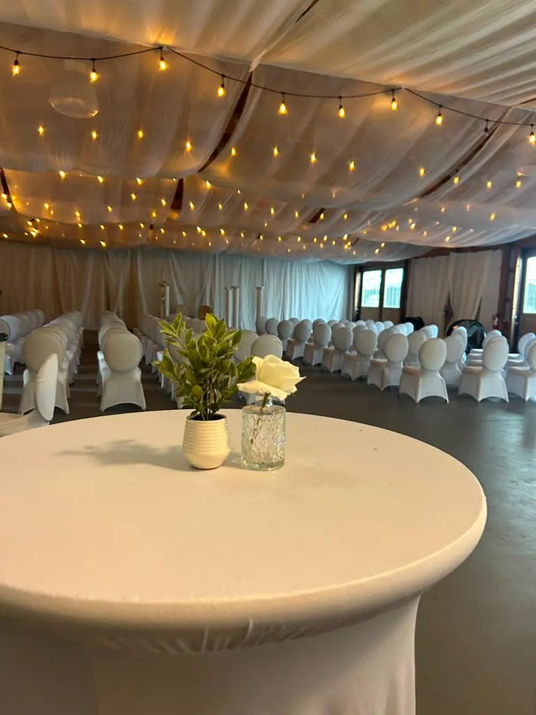 The same room arranged for a ceremony instead of a dinner: rows of white chairs under a draped ceiling threaded with fairy lights.