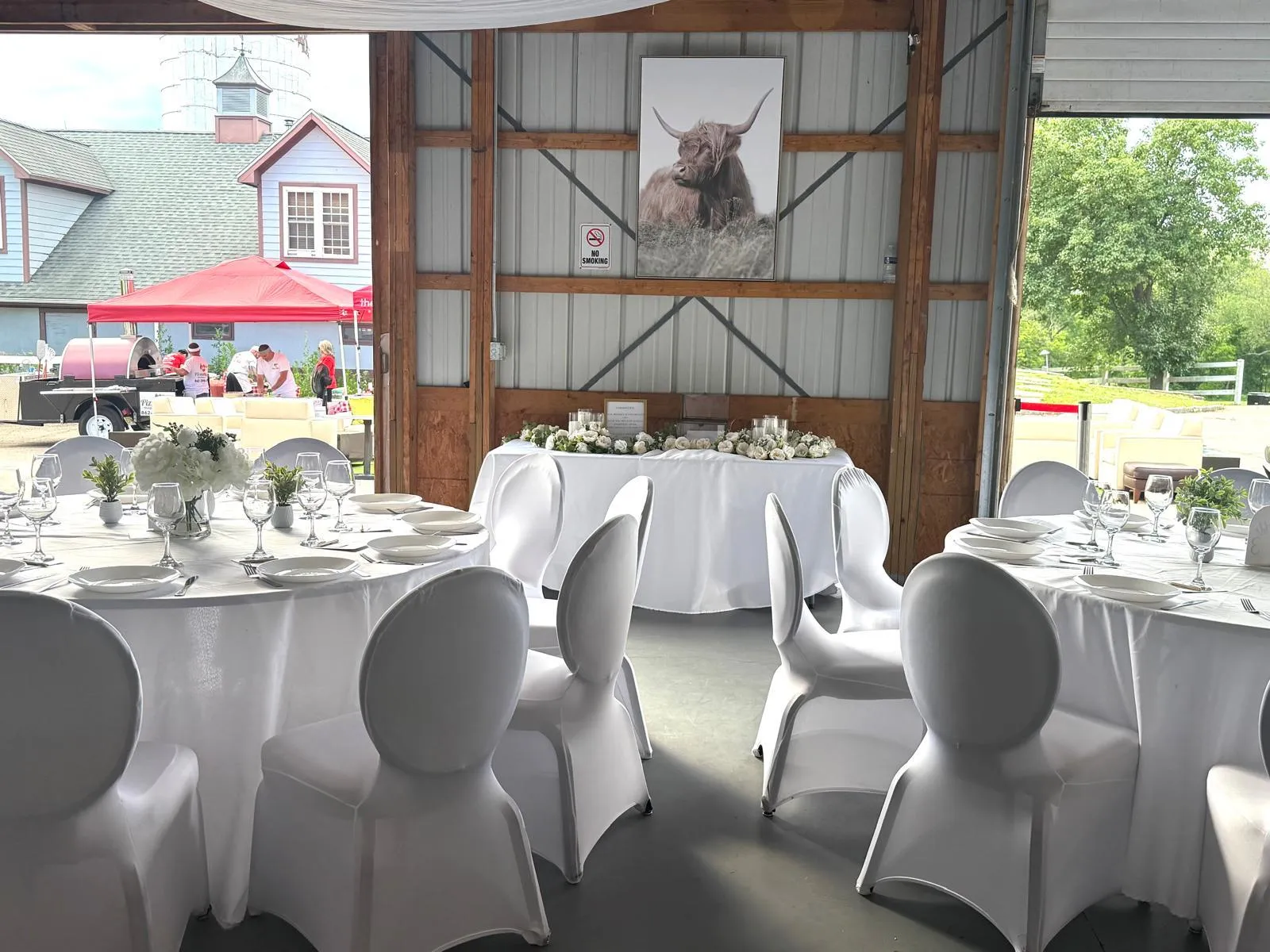 Tables laid in white inside the barn with its doors rolled open to the lawn, an outside caterer working under a canopy beyond.