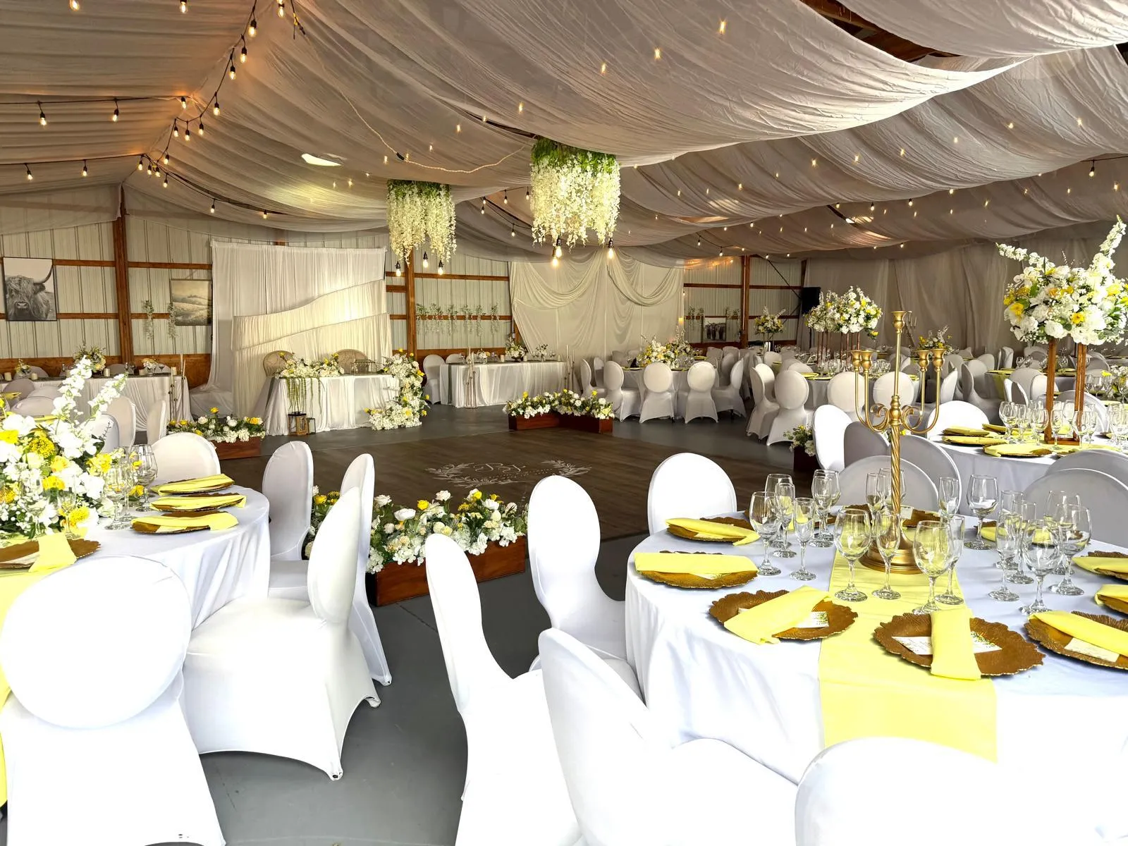 The full reception room: a draped ceiling strung with lights, a dance floor, floral installations and tables laid in yellow, white and gold.