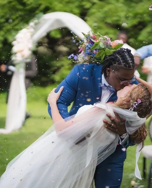 A married couple kiss beneath the ceremony arch as guests throw confetti around them.