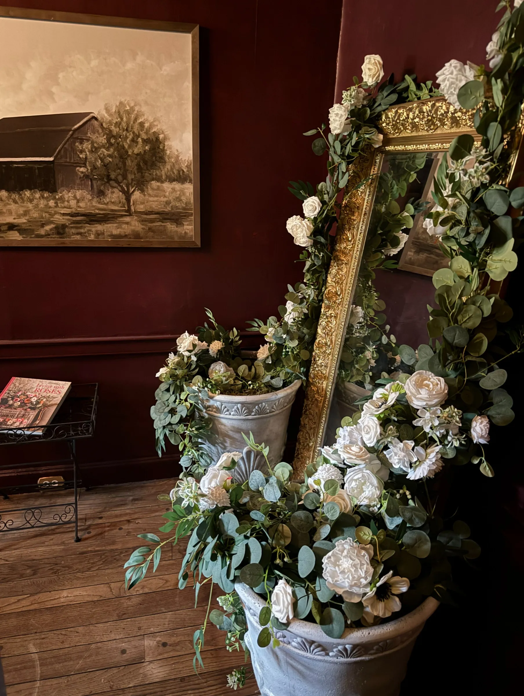 A deep red parlor wall with an antique gold mirror and stone urns of white roses and eucalyptus.